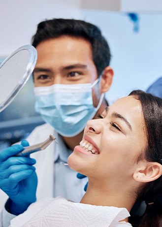 Patient smiling at reflection with dentist and dental hygienist