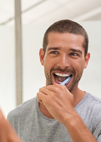 Man smiling while brushing his teeth in bathroom