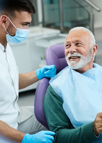 Senior patient looking at dentist while holding small mirror