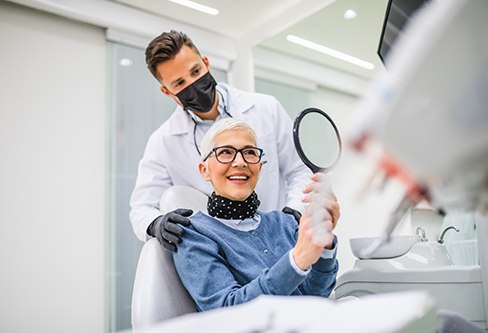 Woman in dental chair smiling into mirror with dentist touching her shoulders