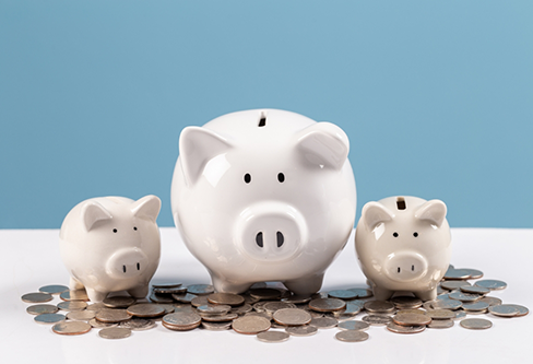 Three piggy banks on a table next to a pile of coins