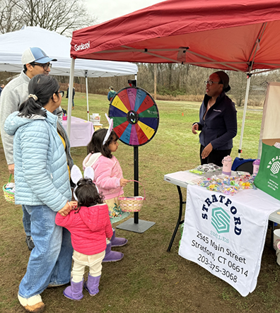 Doctor Sheng with a baby in a stroller by a Stratford Smiles table at a local event
