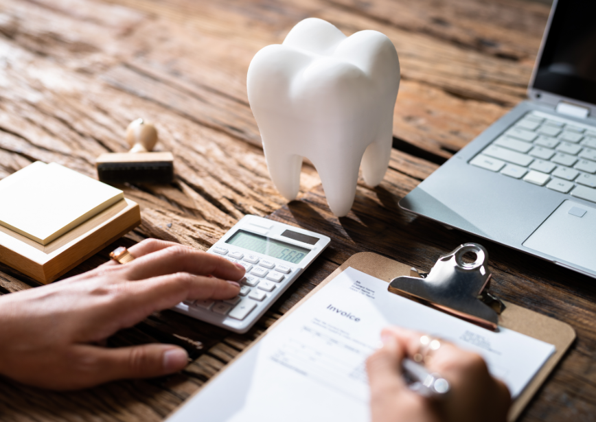 Desk with invoice, calculator, hands writing, laptop, and a model tooth